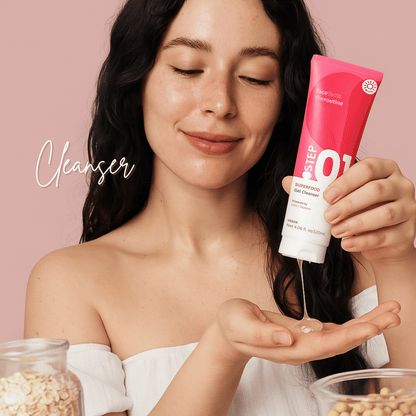 Woman using Superfood Gel Cleanser on palm, clean skin, soft pink background, enriched with oats and soy.