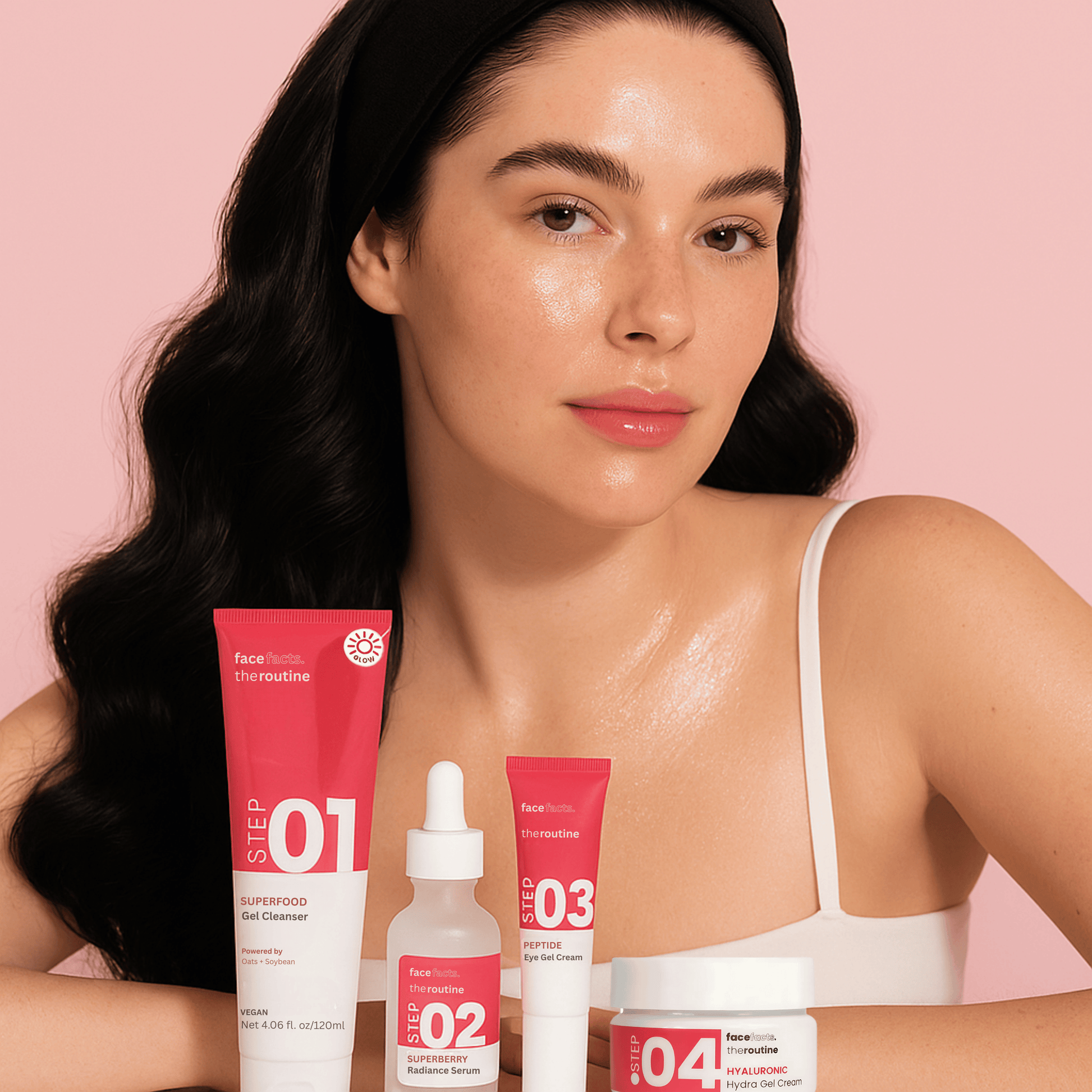 Woman with glowing skin showcasing full Face Facts skincare gift set on pink background for daily glow routine.