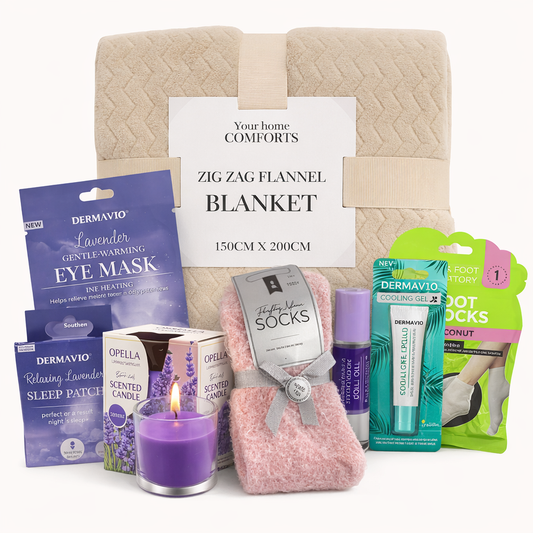 Cozy comfort gift set with soft flannel blanket, lavender eye mask, scented candle, fluffy socks, foot care products and sleep accessories on white background.
