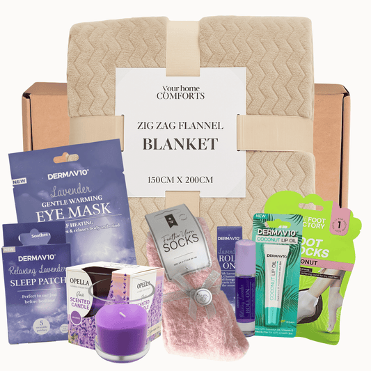 Relaxing spa gift set with flannel blanket, lavender candle, eye mask, sleep patch, socks, lip oil and foot socks arranged on a gift box